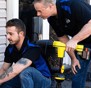 Two Acts of Service Plumbing technicians working a line locator outside a home
