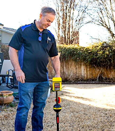 Acts of Service Plumbing technician using a leak locator in a yard